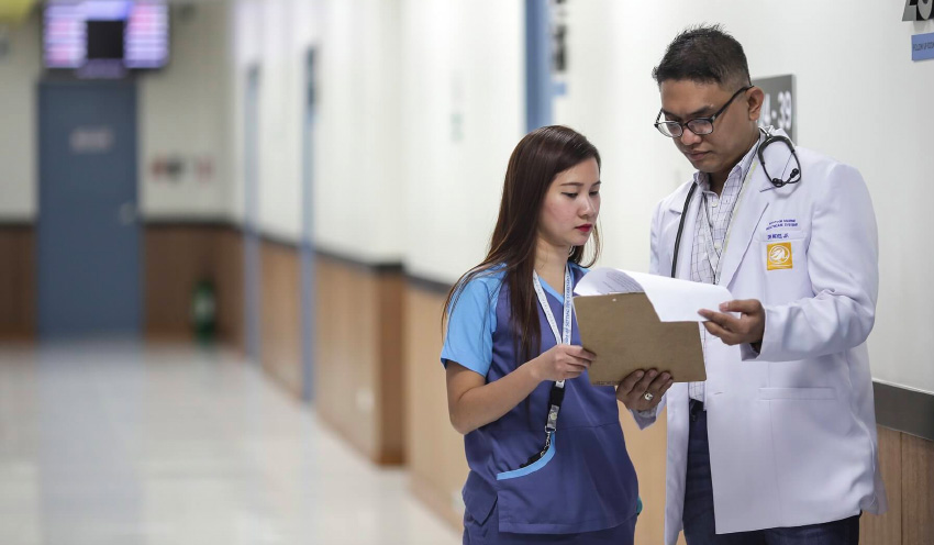 Image with a male and female doctor discussing a patients report in a hospitals corridor